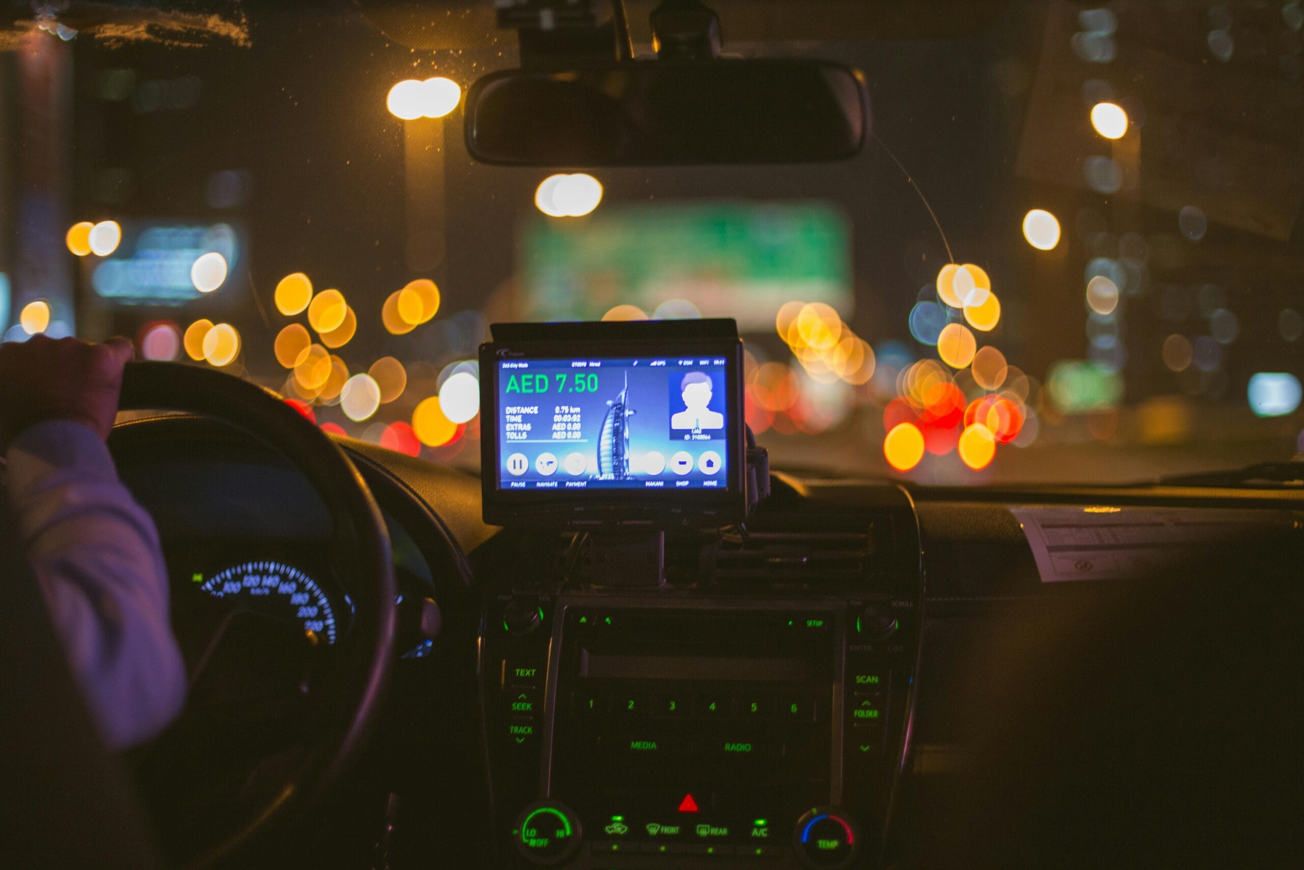 Experience a nighttime taxi ride in Dubai with bokeh city lights and focus on the dashboard and screen.